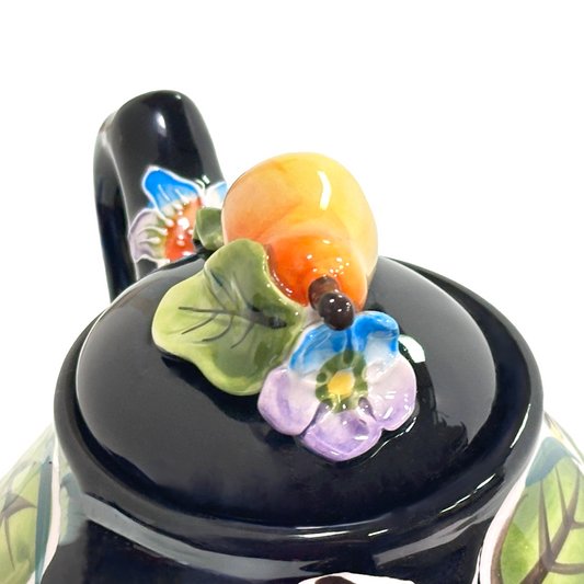 Decorative black teapot with colorful floral designs on a white background
